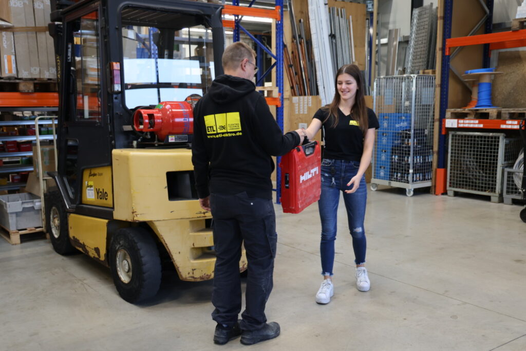 Mitarbeiterin übergibt Servicekoffer an Elektriker.