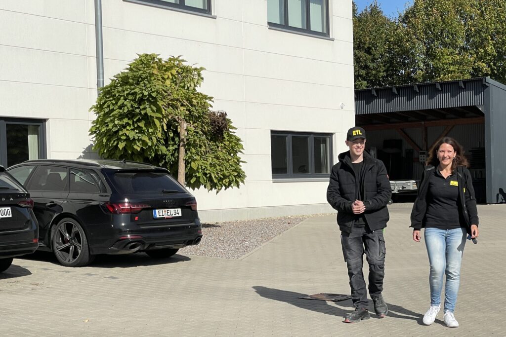Mitarbeiterin und Azubi stehen vor Firmengebäude